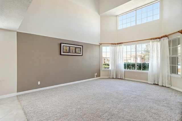 carpeted empty room featuring a wealth of natural light, a towering ceiling, baseboards, and a textured ceiling