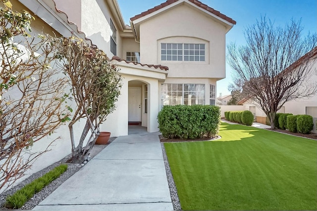 doorway to property with a yard, fence, a tile roof, and stucco siding