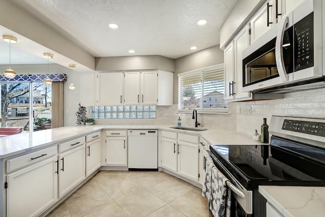 kitchen featuring white appliances, tasteful backsplash, white cabinets, a peninsula, and a sink