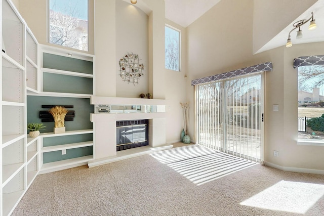 unfurnished living room featuring a wealth of natural light, a high ceiling, a fireplace, and carpet