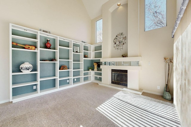 unfurnished room featuring high vaulted ceiling, carpet flooring, and a glass covered fireplace