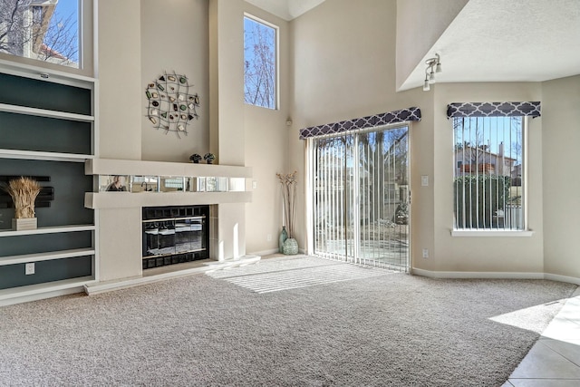 unfurnished living room with carpet, a high ceiling, a glass covered fireplace, a textured ceiling, and baseboards