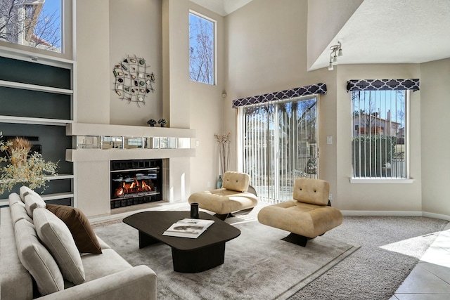 tiled living room with baseboards, a glass covered fireplace, a high ceiling, carpet flooring, and built in shelves