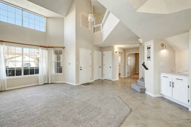 interior space featuring a towering ceiling, light colored carpet, stairway, and baseboards