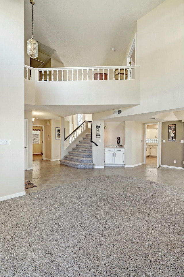 unfurnished living room with visible vents, tile patterned floors, stairs, a high ceiling, and carpet flooring