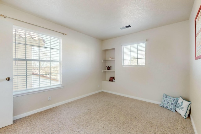 unfurnished room featuring a textured ceiling, carpet floors, visible vents, and baseboards