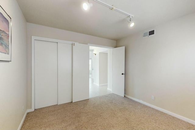 unfurnished bedroom with carpet floors, a closet, visible vents, track lighting, and baseboards