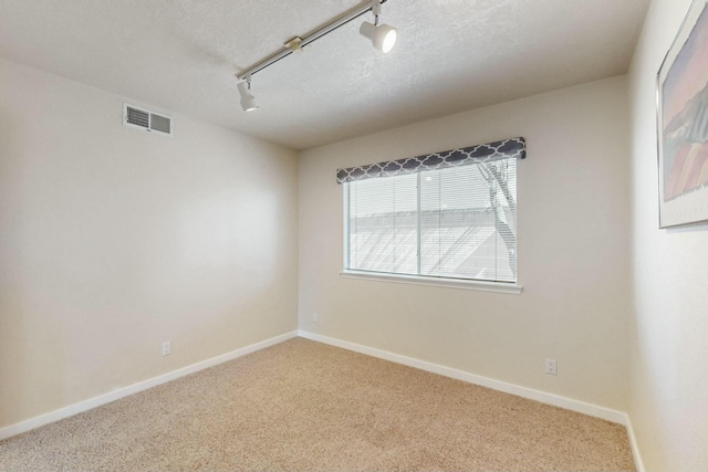 carpeted spare room featuring rail lighting, visible vents, a textured ceiling, and baseboards