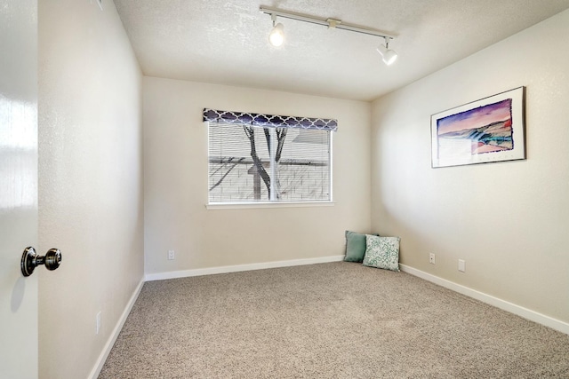 carpeted empty room with a textured ceiling, rail lighting, and baseboards