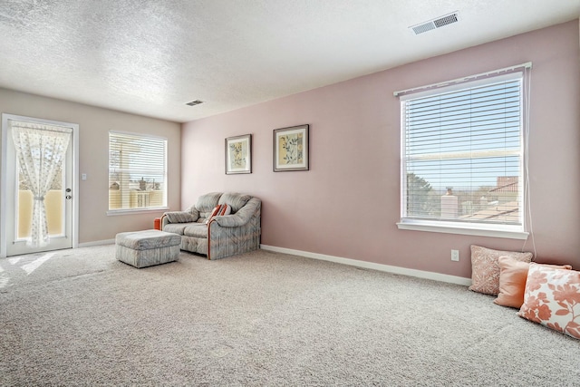 living area with a textured ceiling, carpet, visible vents, and baseboards