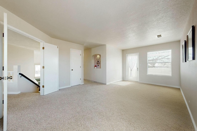 unfurnished room featuring baseboards, visible vents, a textured ceiling, and light colored carpet