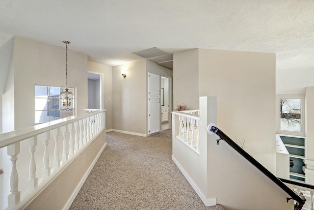 hall featuring light carpet, baseboards, an inviting chandelier, a textured ceiling, and an upstairs landing