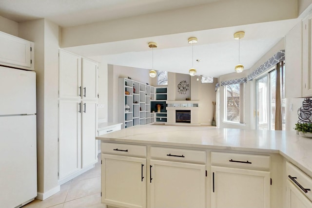 kitchen with light tile patterned floors, hanging light fixtures, freestanding refrigerator, light stone countertops, and a glass covered fireplace