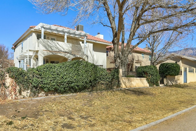 view of front facade with a balcony, a tile roof, a chimney, and stucco siding