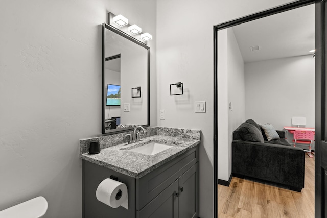 half bathroom with toilet, visible vents, wood finished floors, and vanity