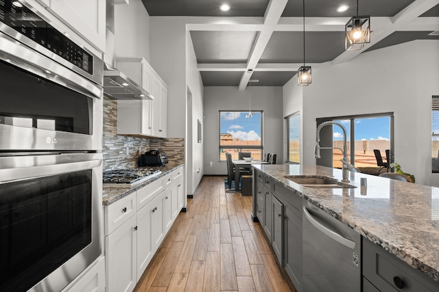 kitchen featuring light wood finished floors, tasteful backsplash, coffered ceiling, appliances with stainless steel finishes, and a sink