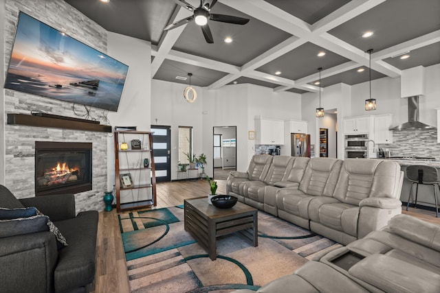 living area featuring a high ceiling, a ceiling fan, wood finished floors, coffered ceiling, and beamed ceiling