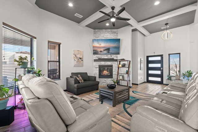 living area featuring a stone fireplace, coffered ceiling, wood finished floors, visible vents, and a towering ceiling