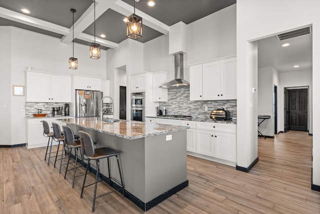 kitchen featuring light wood finished floors, visible vents, wall chimney exhaust hood, appliances with stainless steel finishes, and a sink