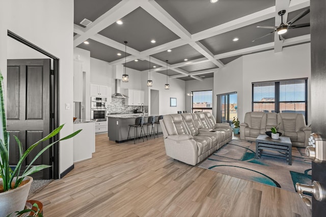 living room with light wood-style floors, a high ceiling, and beamed ceiling