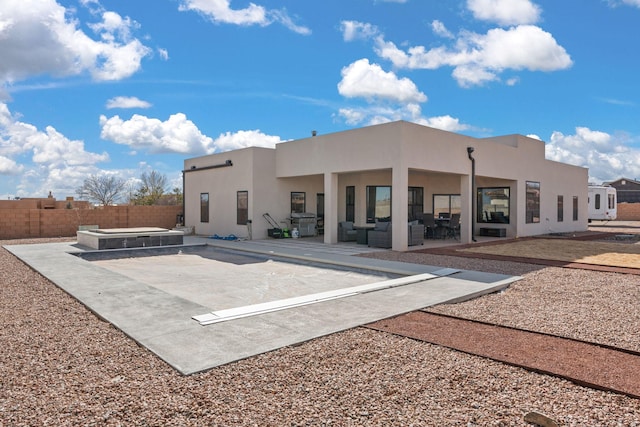 rear view of property featuring a patio, stucco siding, an outdoor hangout area, an in ground hot tub, and a fenced backyard