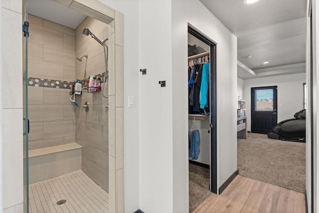 full bath featuring a walk in closet, a shower stall, baseboards, and wood finished floors