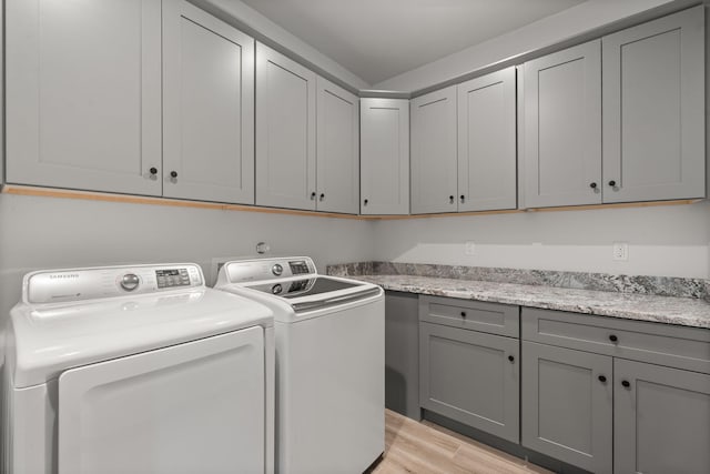 washroom featuring light wood-style floors, washing machine and dryer, and cabinet space