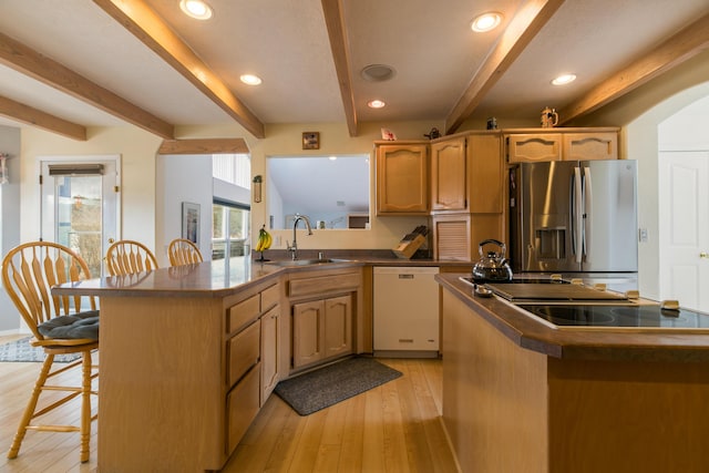 kitchen featuring a breakfast bar, a sink, dark countertops, stainless steel fridge, and dishwasher