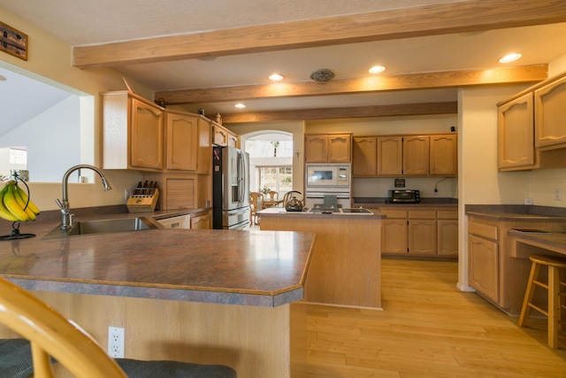 kitchen with white microwave, a peninsula, stainless steel fridge with ice dispenser, a sink, and dark countertops