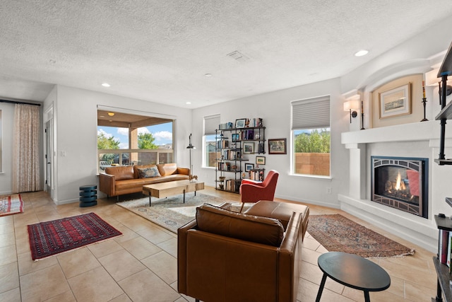 tiled living area with a glass covered fireplace, recessed lighting, baseboards, and a textured ceiling