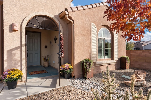 view of exterior entry featuring stucco siding and fence