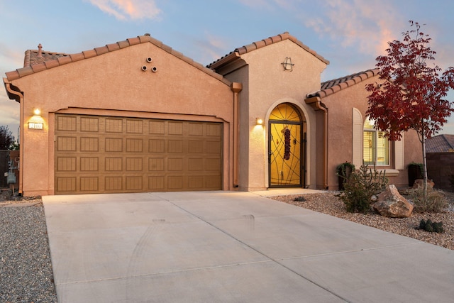 mediterranean / spanish-style house with a garage, concrete driveway, stucco siding, and a tiled roof