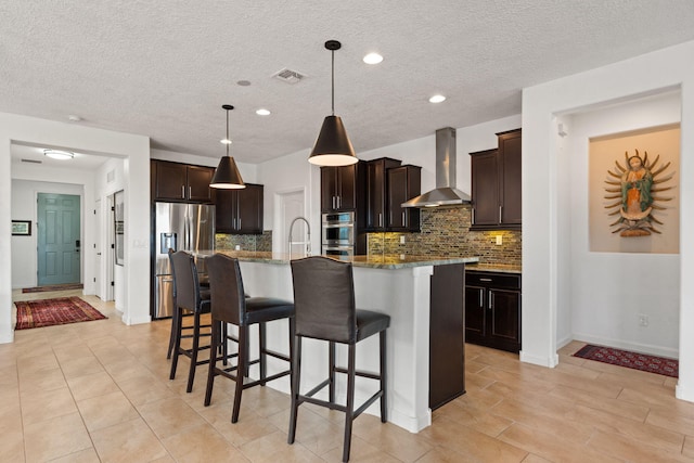 kitchen with a kitchen bar, visible vents, stainless steel appliances, dark brown cabinetry, and wall chimney exhaust hood