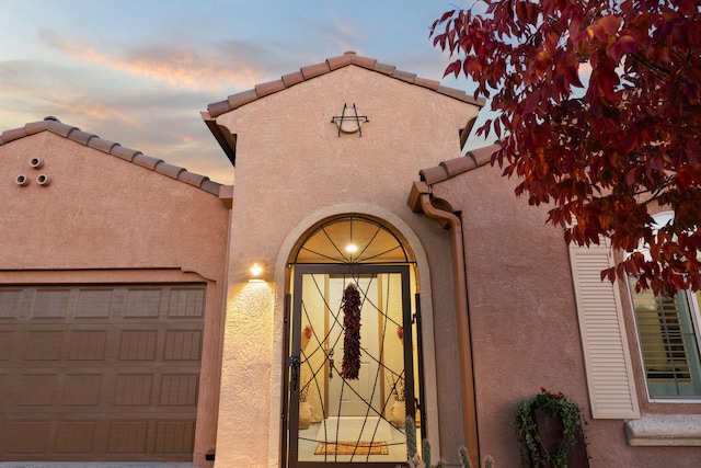 view of exterior entry with stucco siding, a tiled roof, and a garage