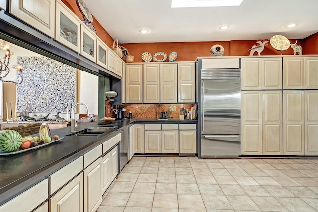 kitchen with stainless steel built in refrigerator, light tile patterned flooring, dark countertops, and a sink