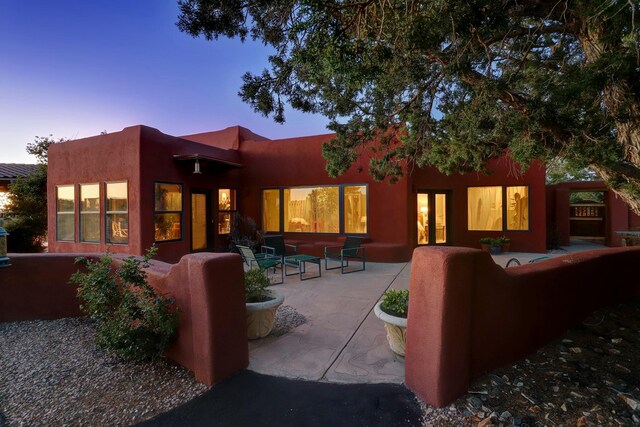 7 Calle Cholla, Placitas, NM 87043 - back of house at dusk featuring an outdoor living space, a patio area, and stucco siding