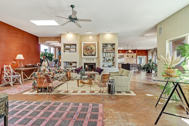 living area with a ceiling fan, visible vents, a skylight, a fireplace, and brick floor