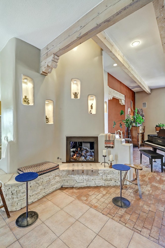 tiled living room featuring beam ceiling, a textured ceiling, and a stone fireplace