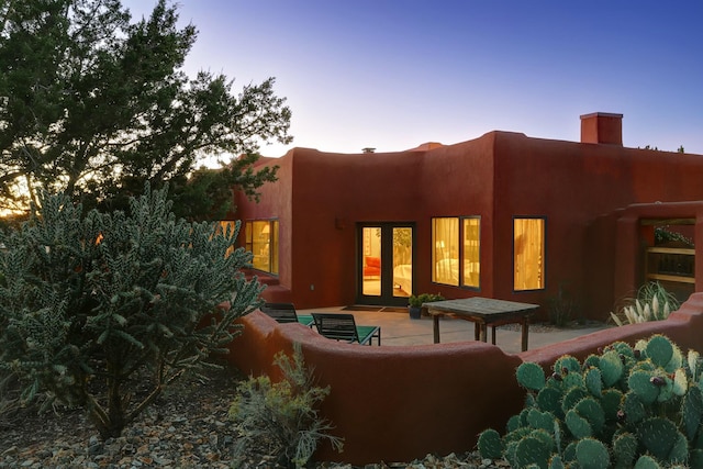 back of property at dusk with french doors, an outdoor hangout area, and a patio area