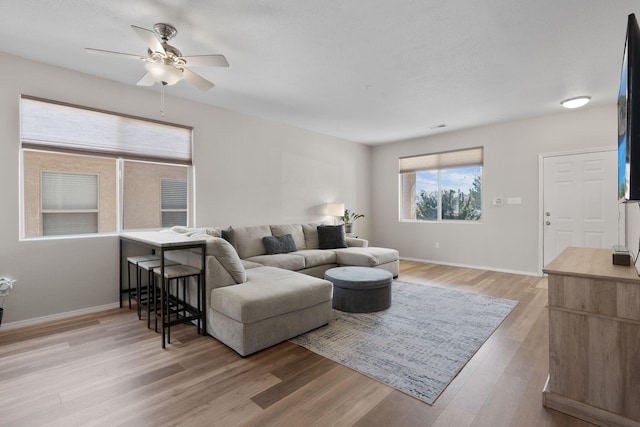 living area with light wood finished floors, a ceiling fan, and baseboards