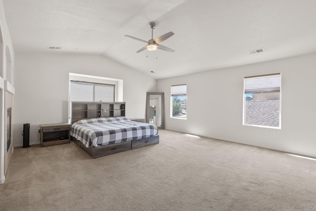 carpeted bedroom featuring a textured ceiling, visible vents, vaulted ceiling, and a ceiling fan