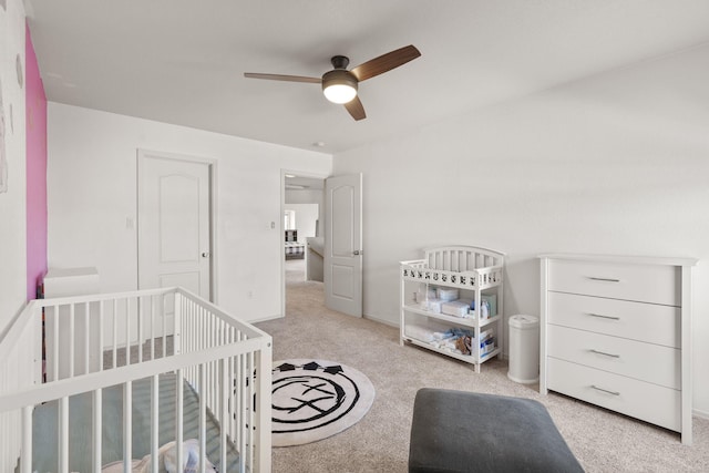 carpeted bedroom featuring a crib and a ceiling fan