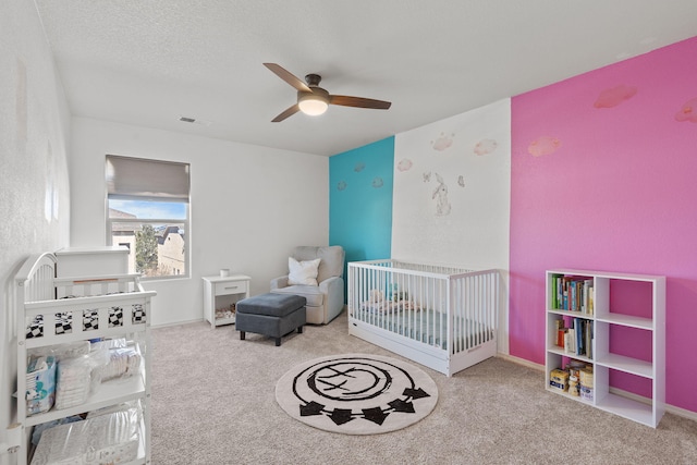 bedroom with carpet floors, a crib, visible vents, and a ceiling fan