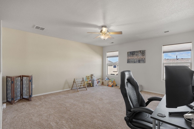 carpeted office space featuring baseboards, ceiling fan, visible vents, and a textured ceiling