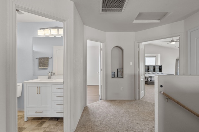 corridor with visible vents, attic access, light carpet, a sink, and an upstairs landing