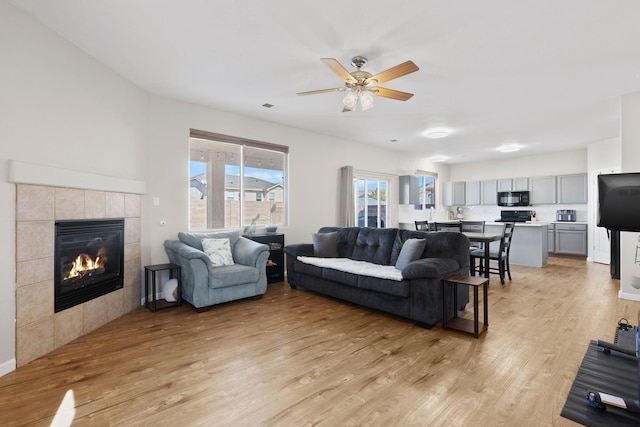 living room with light wood-style floors, a fireplace, and a ceiling fan