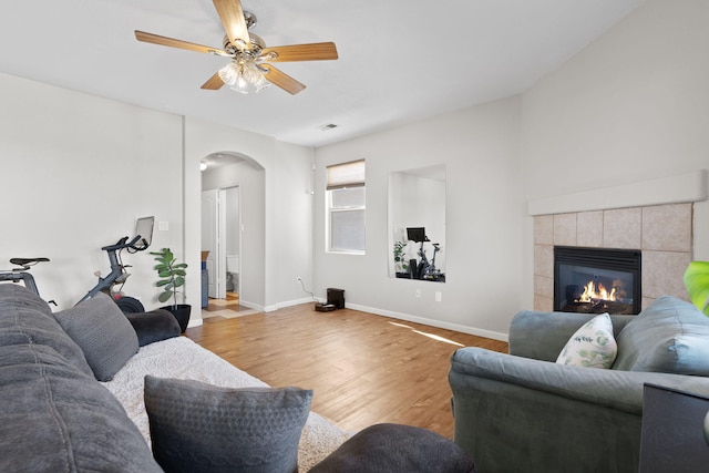 living room with arched walkways, a fireplace, ceiling fan, wood finished floors, and baseboards