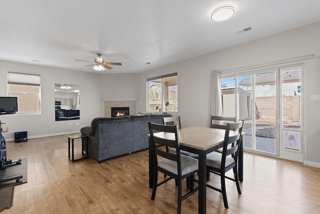 dining area with light wood finished floors, baseboards, visible vents, a ceiling fan, and a fireplace