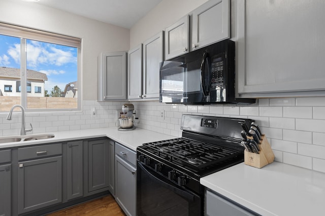 kitchen with tasteful backsplash, light countertops, gray cabinetry, a sink, and black appliances