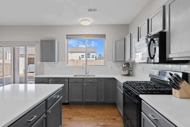 kitchen featuring tasteful backsplash, visible vents, gas range, gray cabinetry, and a sink